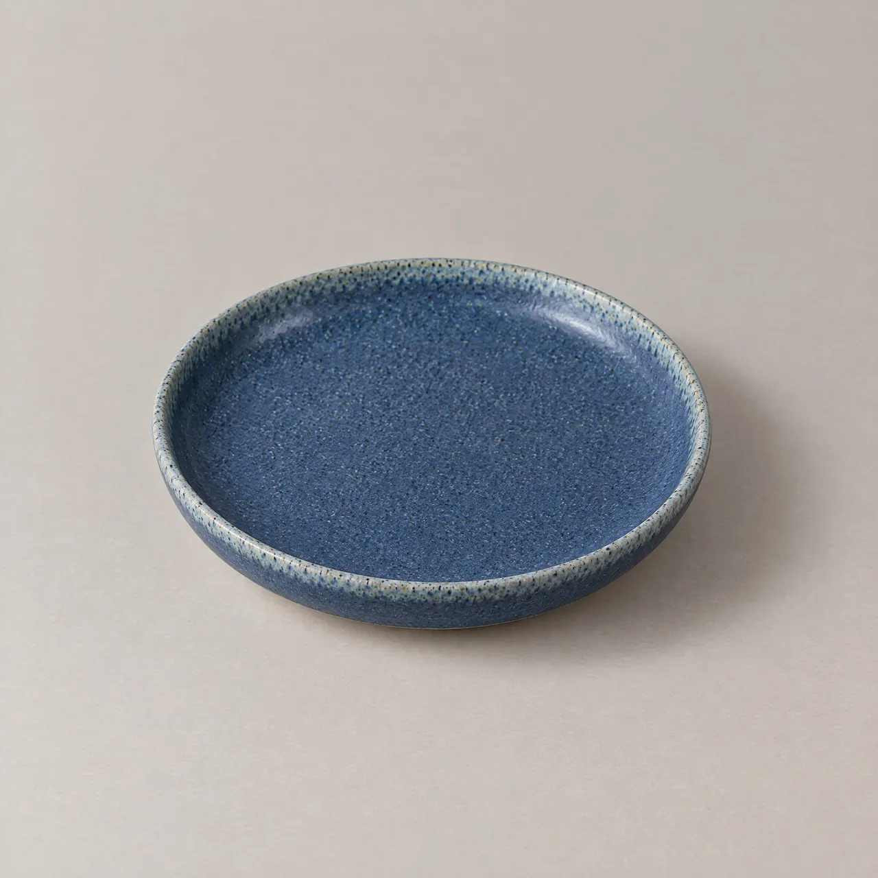 Assiette plate en grès émaillé bleu vue du dessus sur fond gris clair