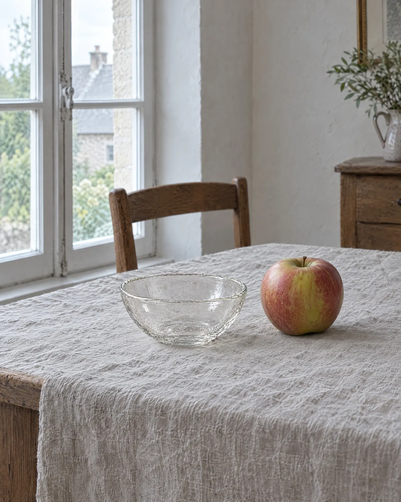 Coupelle en verre soufflé posée sur une nappe en lin à côté d'une pomme rouge, près de la fenêtre