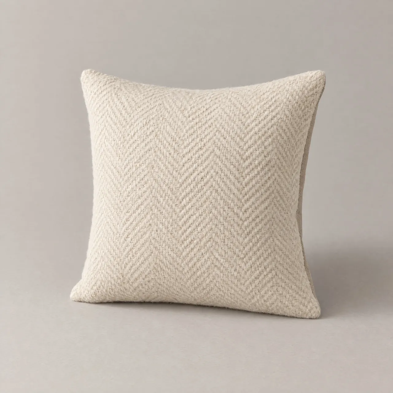 Coussin en laine tissée écrue à chevrons posé debout sur fond gris clair
