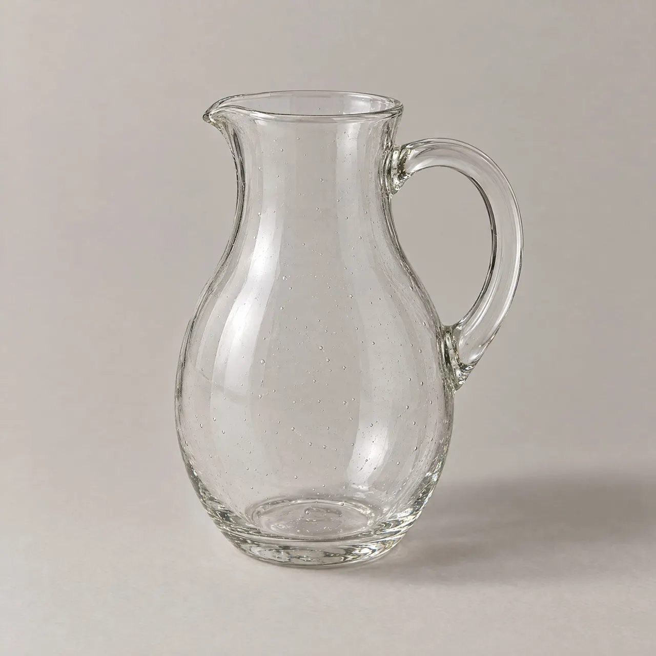 Pichet en verre soufflé transparent avec anse, vu de trois quarts sur fond gris clair