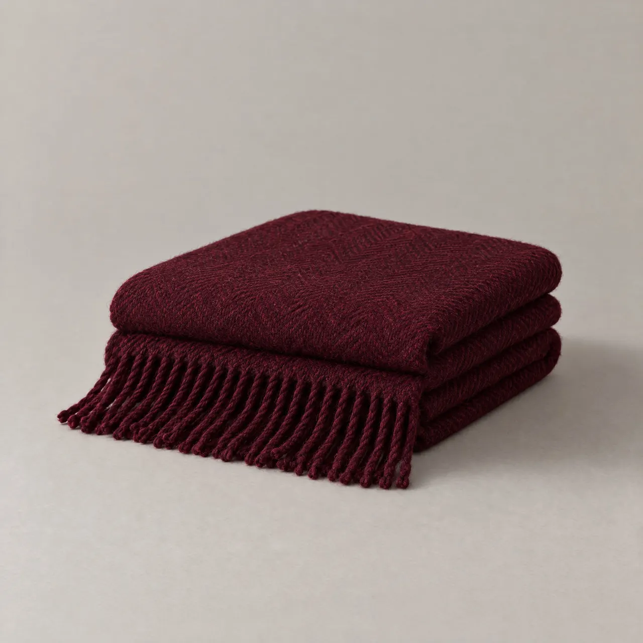Plaid en laine grenat plié en trois, franges visibles, sur fond gris clair