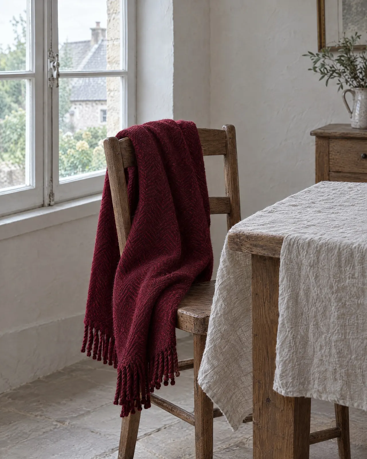 Plaid en laine grenat posé sur le dossier d'une chaise en bois près de la fenêtre