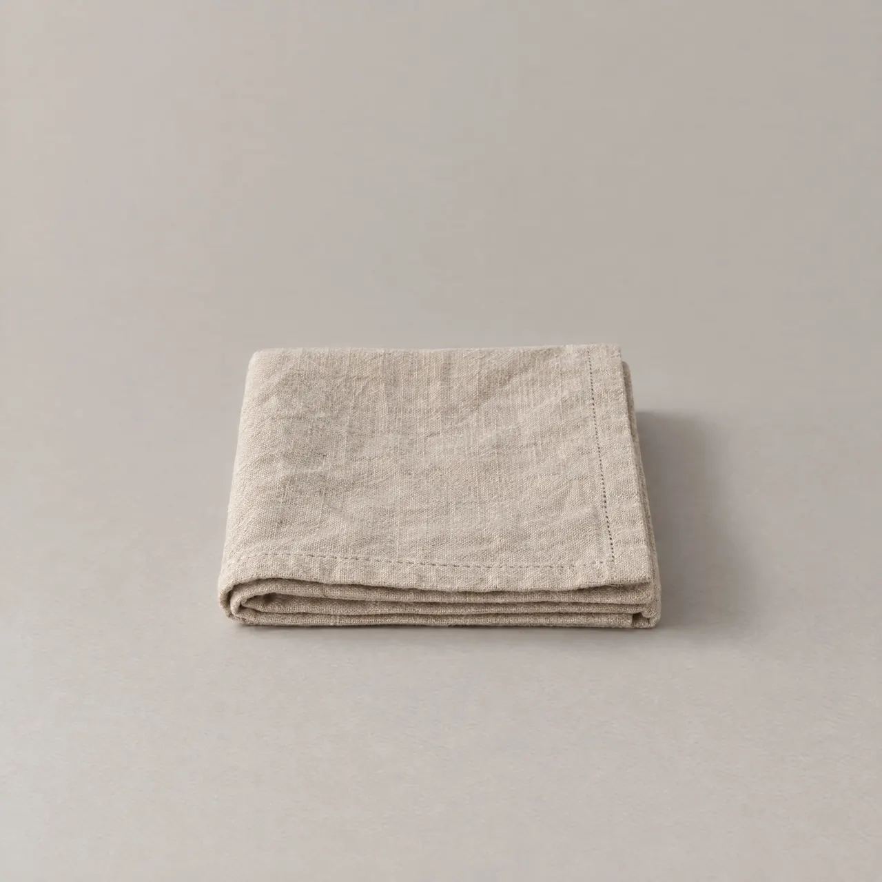 Serviette de table en lin naturel pliée en carré sur fond gris clair