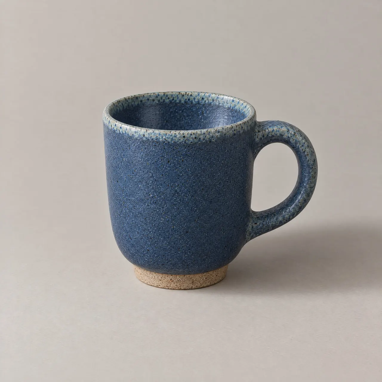 Tasse en grès émaillé bleu avec son anse, vue de trois quarts sur fond gris clair