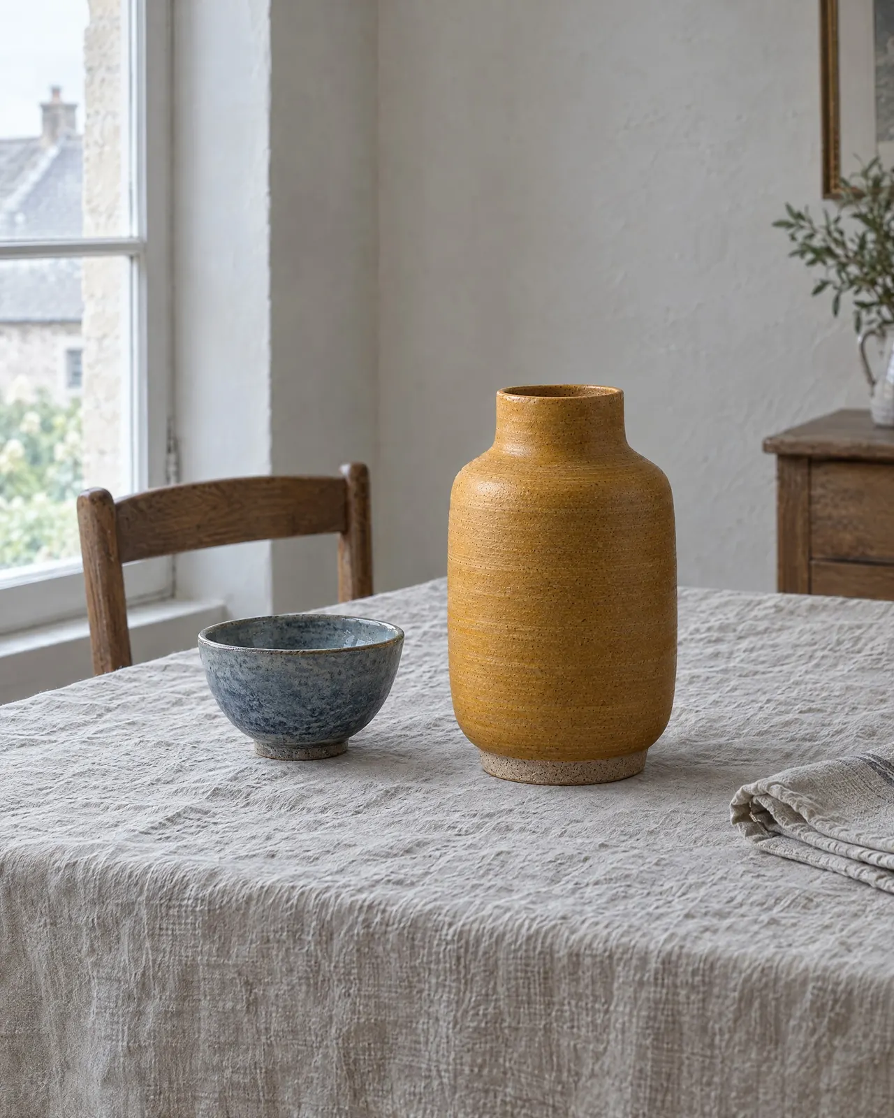 Vase en grès ocre posé sur une nappe en lin à côté d'un bol en grès bleu